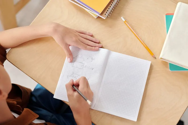 Secondary school student writing mathematical equations on graph paper in a notebook