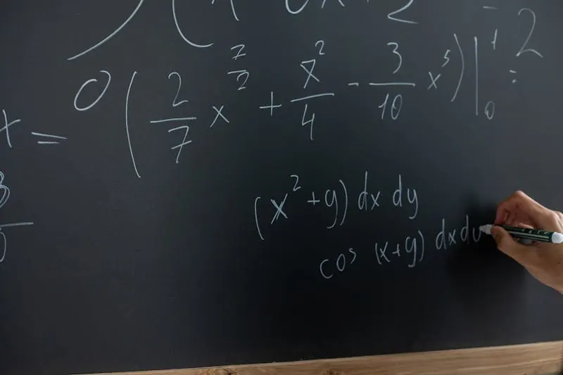 Close-up of hand writing calculus integrals and trigonometric equations on blackboard during tutoring session